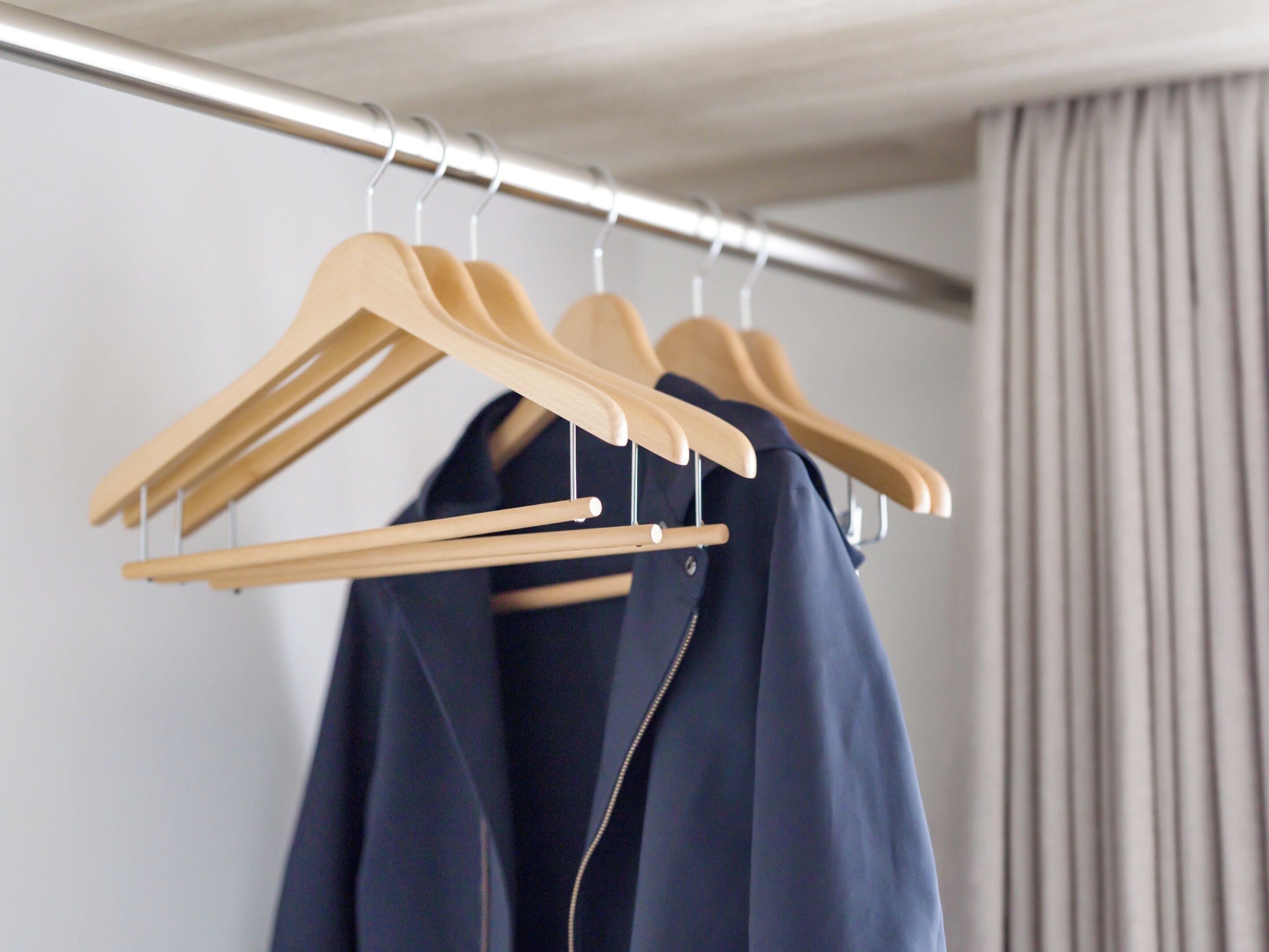 A clothing rack with wooden hangers holding a navy blue coat.