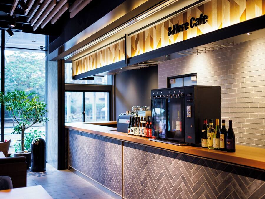 A modern cafe interior with a wooden counter, a coffee machine, and a wine cooler displaying various bottles.