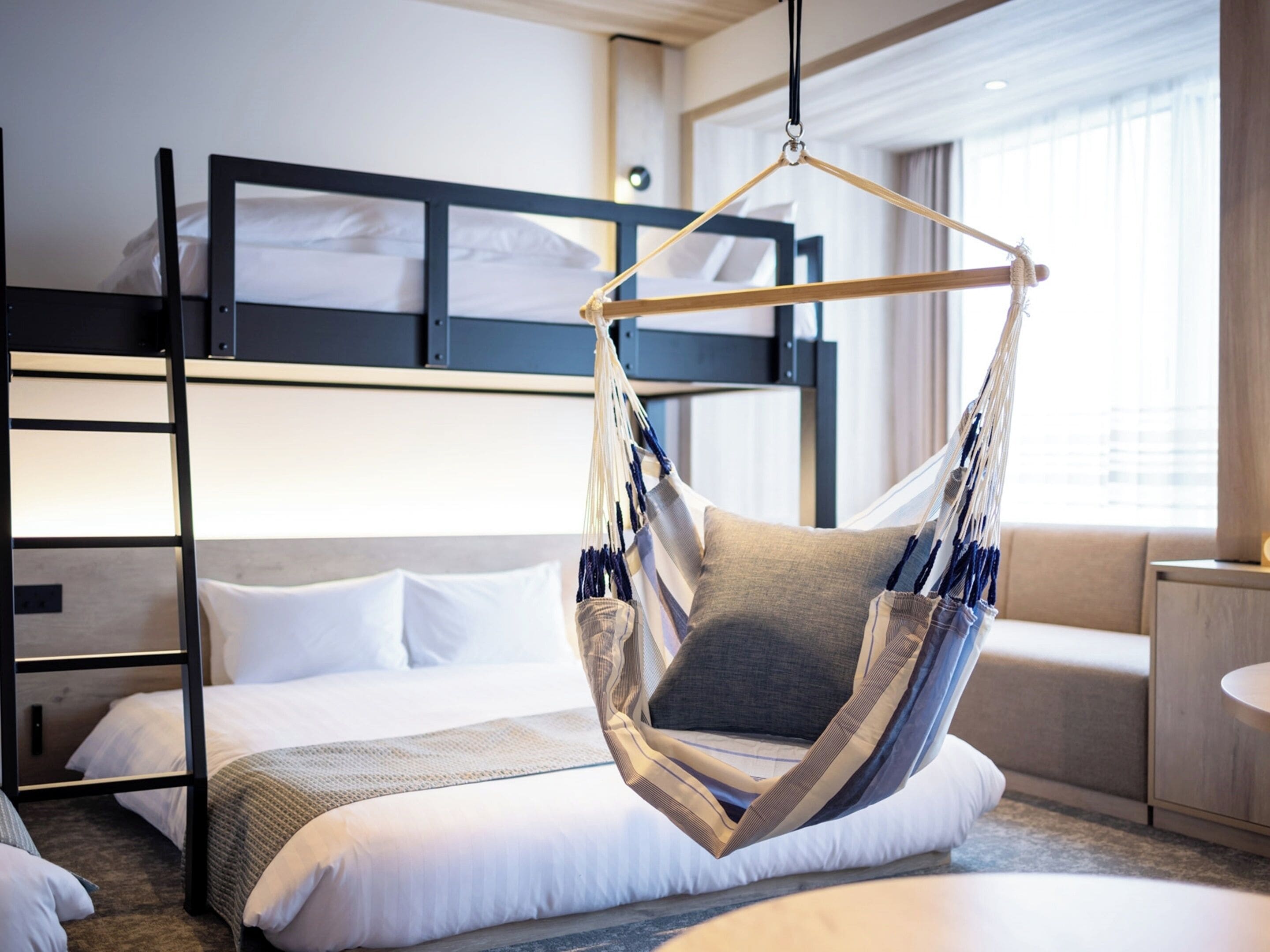 A modern hotel room with a bunk bed, a hanging chair, and a sofa.