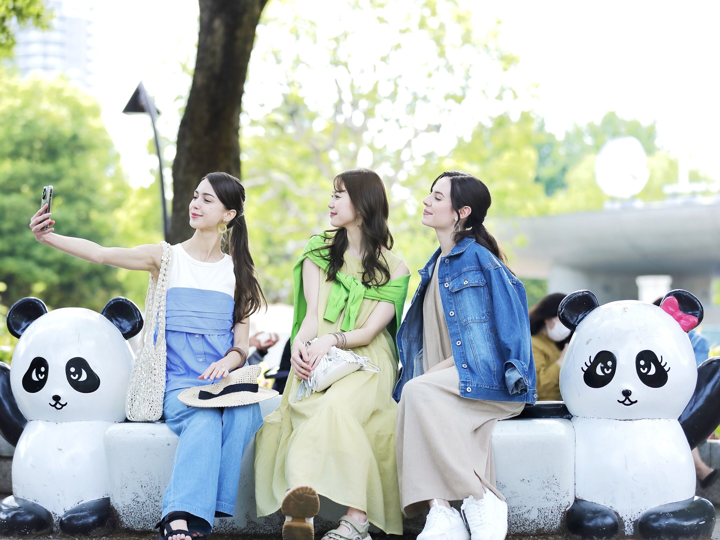 Tres personas sentadas en un banco con esculturas de pandas a cada lado.