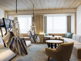 A modern hotel room with a sofa, armchairs, a hanging chair, a TV, and a window with curtains.