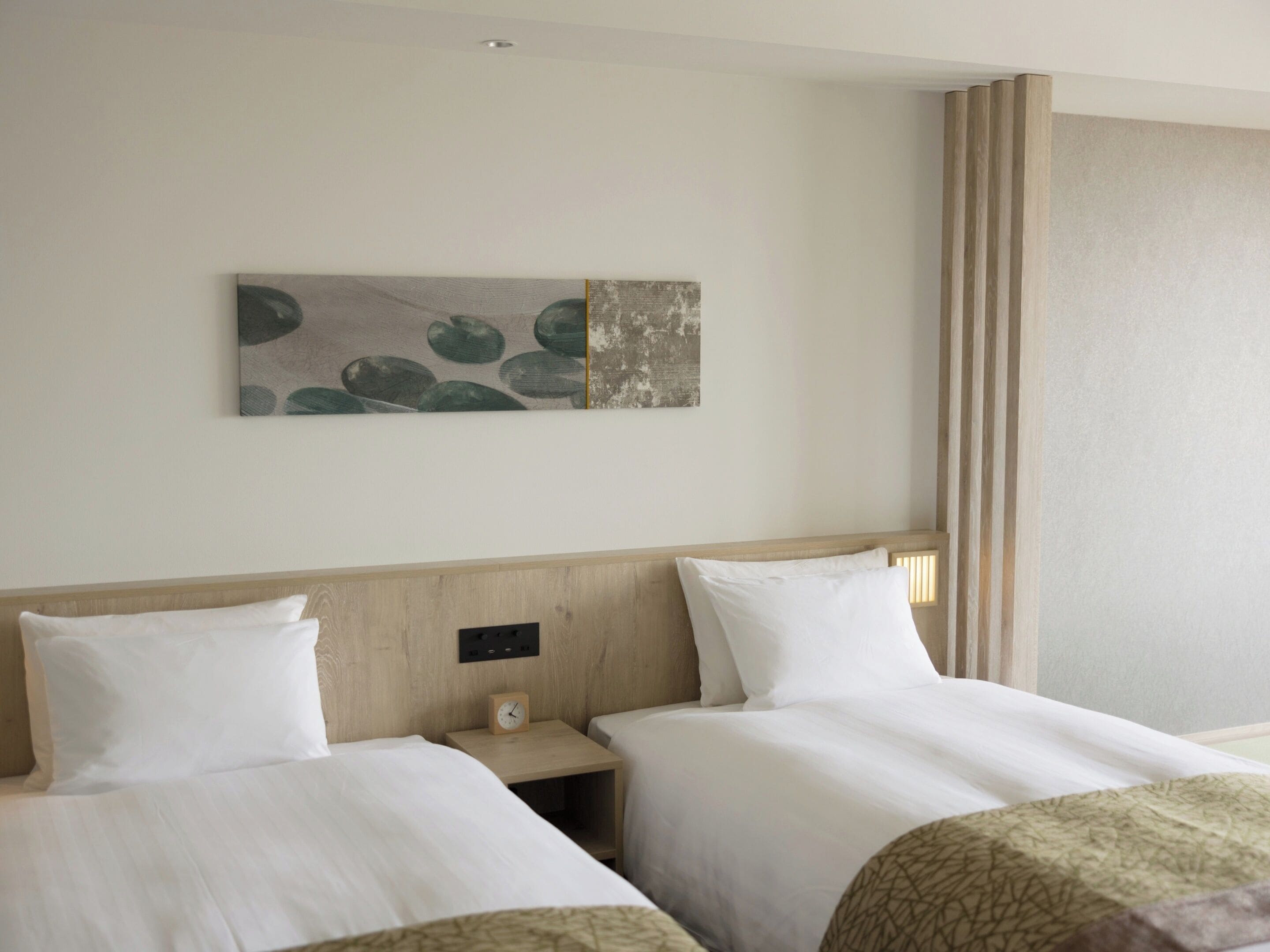 A hotel room with two beds, a wooden headboard, a nightstand with a clock, and a wall-mounted artwork.