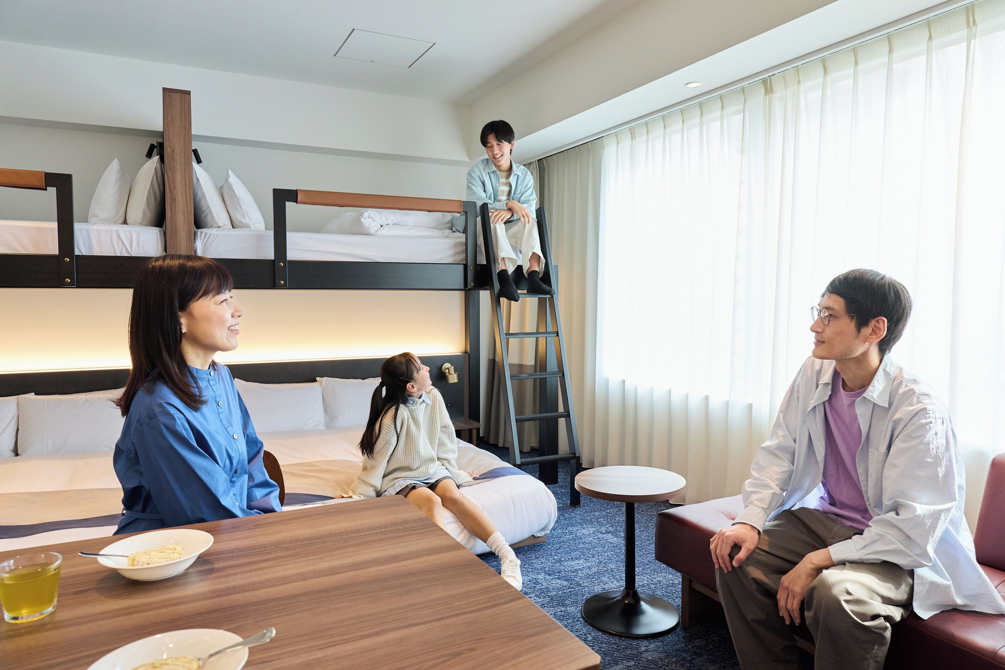 A hotel room with bunk beds, a dining table, a small round table, and a ladder.
