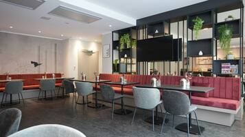 Een modern restaurant met een rode, beklede bank, grijze stoelen en een zwart, aan de muur bevestigd televisiescherm.