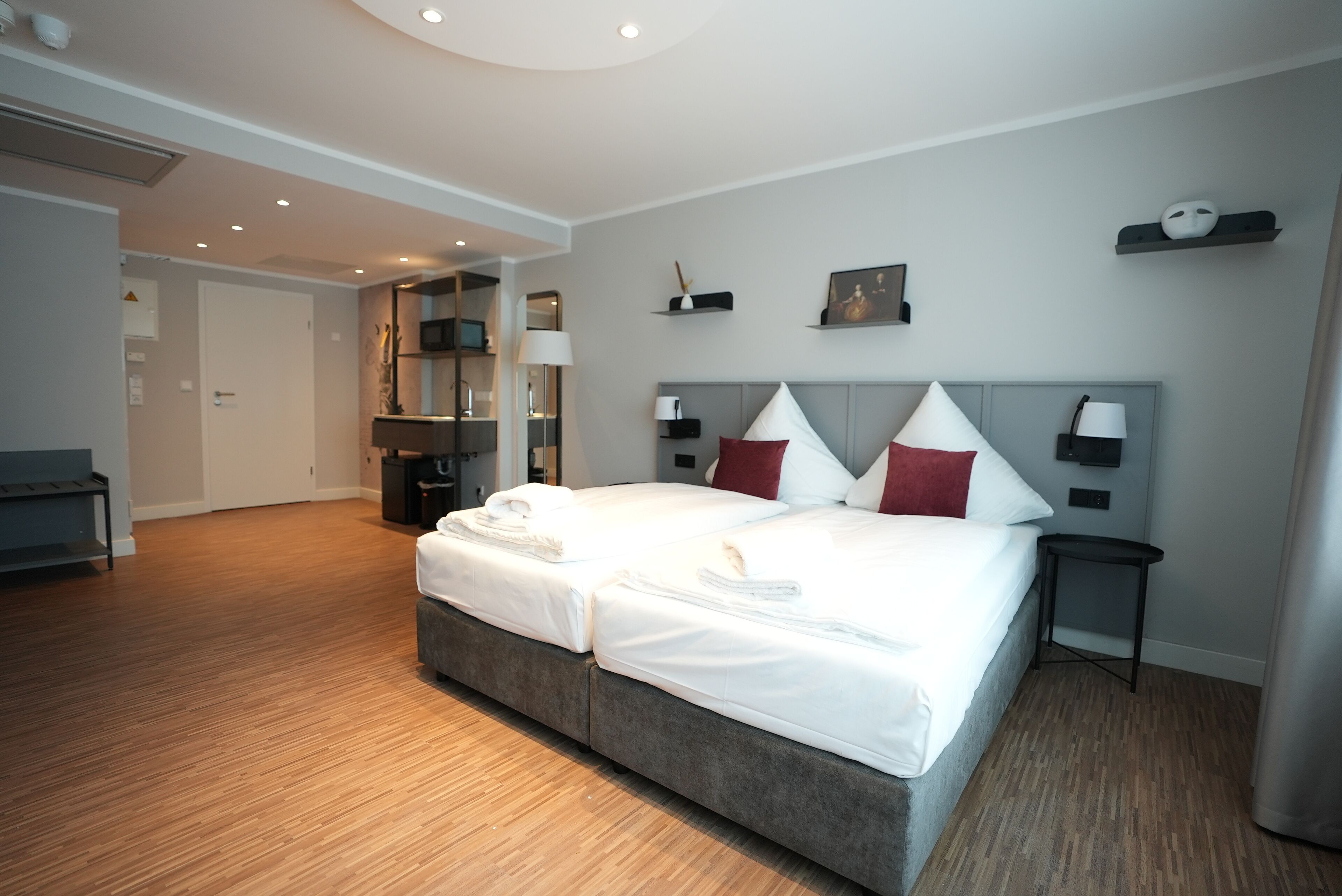 A modern hotel room with a large bed, a desk, and a wardrobe.