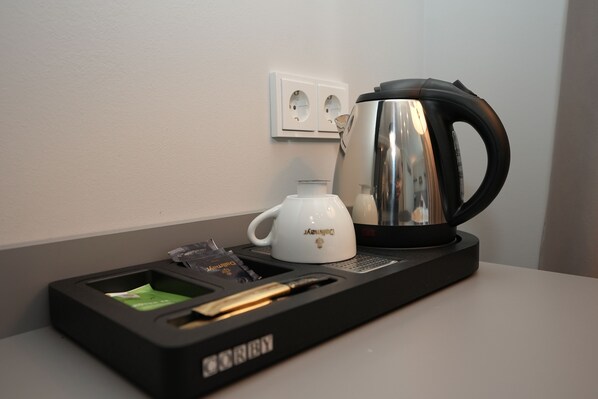 A coffee maker, a white mug, and a tray with a pen and a packet of sugar on a table. - Boutique Kaiser - Hotel & Apartments (Frankfurt)