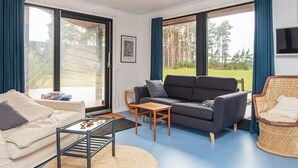 A cozy living room with a sofa, a small table, and a wicker chair. There is a framed picture on the wall and a large window with curtains. - 6 Person Holiday Home in Ebeltoft-by Traum (Ebeltoft)