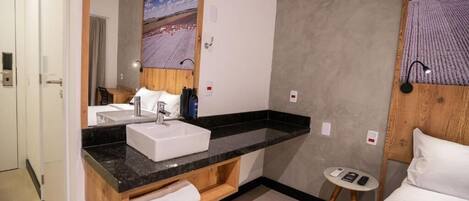 A modern bathroom with a large mirror, a sink, and a small table with a remote control.