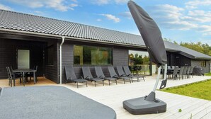 A modern building with a tiled roof, outdoor seating with chairs and tables, and a covered area with a table and chairs. - 14 Person Holiday Home in Ebeltoft-by Traum (Ebeltoft)