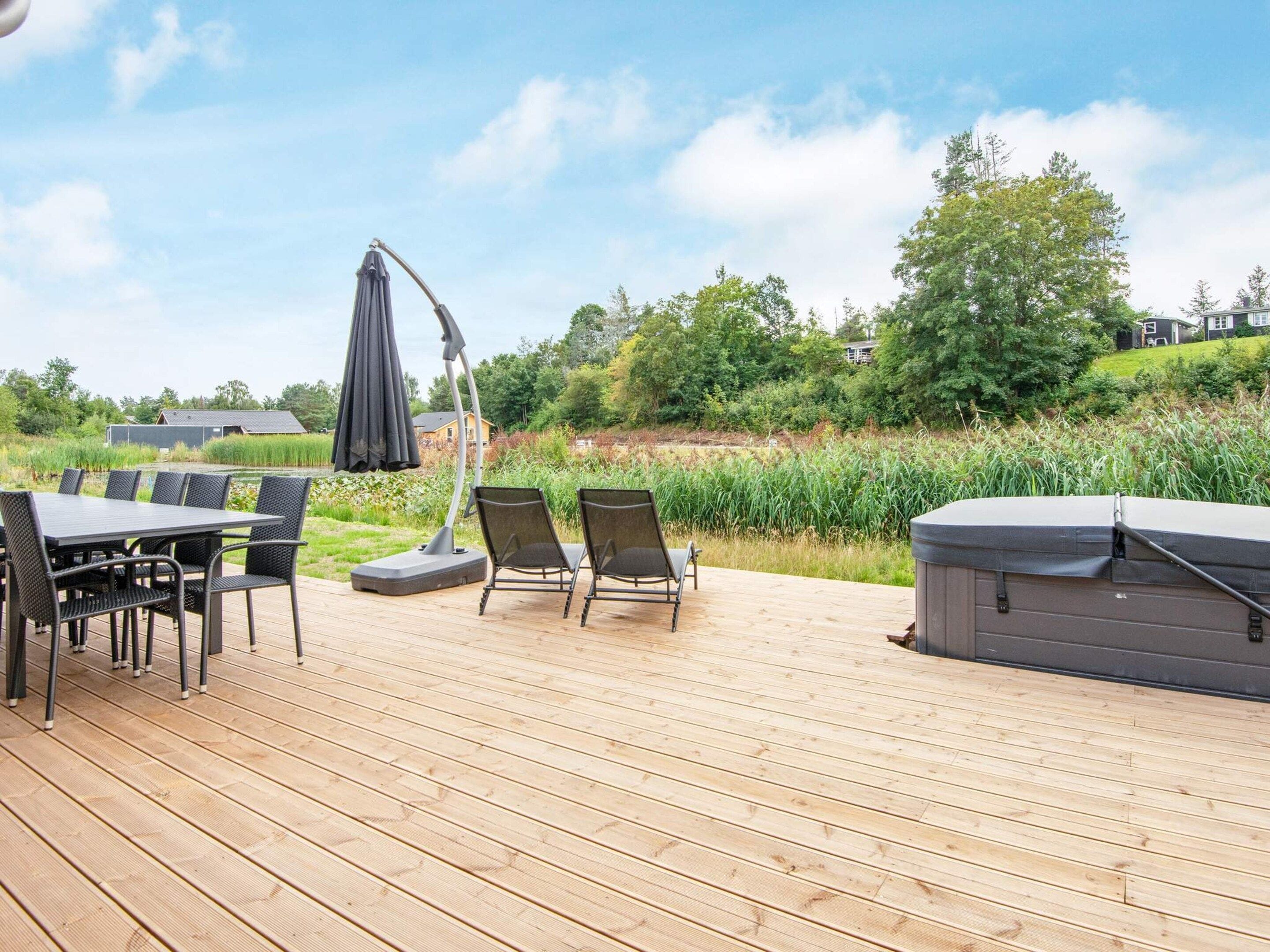 Una terraza de madera con una mesa, sillas, una sombrilla y un jacuzzi.