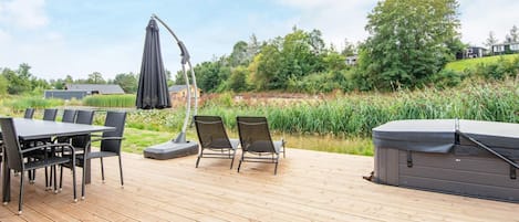 Une terrasse en bois avec une table et des chaises, un parasol et un jacuzzi.