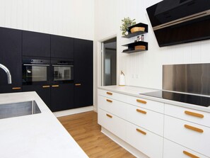 A modern kitchen with black cabinets, a stainless steel range hood, and a white countertop. - 5 Star Holiday Home in Ebeltoft (Ebeltoft)