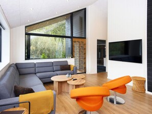 A modern living room with a sectional sofa, two round wooden tables, and orange chairs. - 5 Star Holiday Home in Ebeltoft (Ebeltoft)