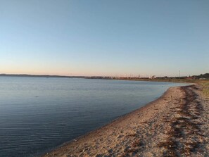 A calm body of water with a sandy shore and distant buildings. - 5 Star Holiday Home in Ebeltoft (Ebeltoft)