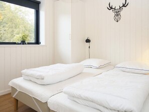 A bedroom with two beds, a window with a view of trees, a wall-mounted deer head decoration, and a bedside table with a lamp. - 5 Star Holiday Home in Ebeltoft (Ebeltoft)