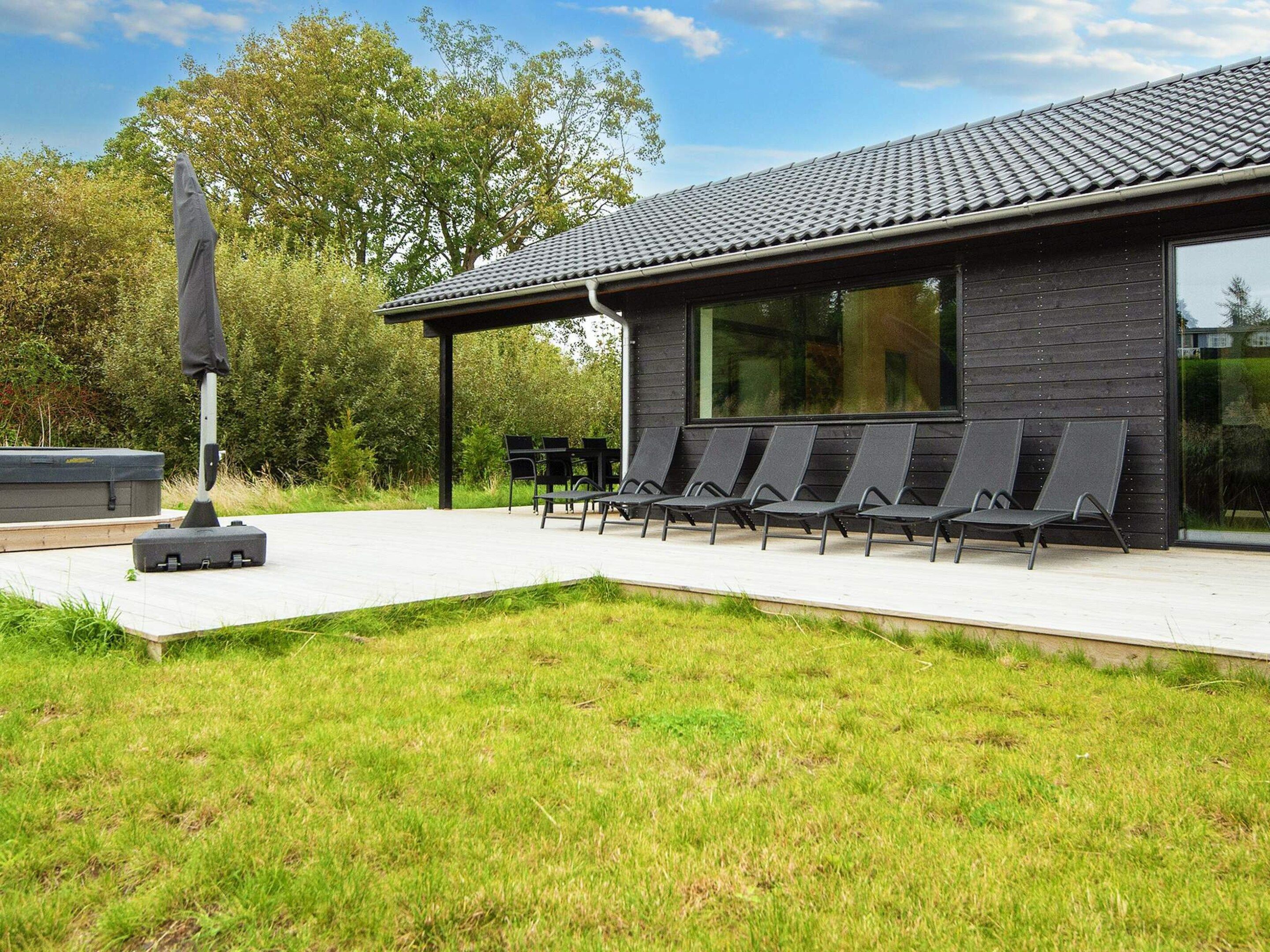 A modern building with a flat roof, a covered outdoor seating area with chairs, and a large window.