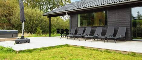 A modern building with a flat roof, a covered outdoor seating area with chairs, and a large window.