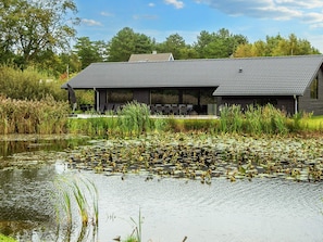 A modern building with a sloped roof, surrounded by a body of water with lily pads. - 5 Star Holiday Home in Ebeltoft (Ebeltoft)
