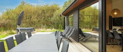 An outdoor dining area with a table and chairs, a grill, and a view of the surrounding forest.