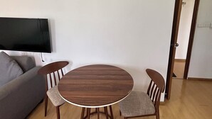 A living room with a round wooden table and four chairs, a grey sofa, and a flat-screen TV mounted on the wall.