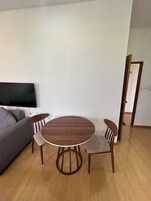 Uma sala de estar com uma mesa redonda de madeira e quatro cadeiras, um sofá cinza e uma TV de tela plana fixada na parede.