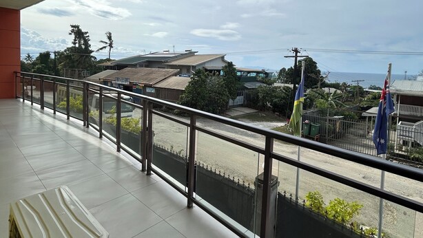 A balcony with a view of a street, buildings, and flags.