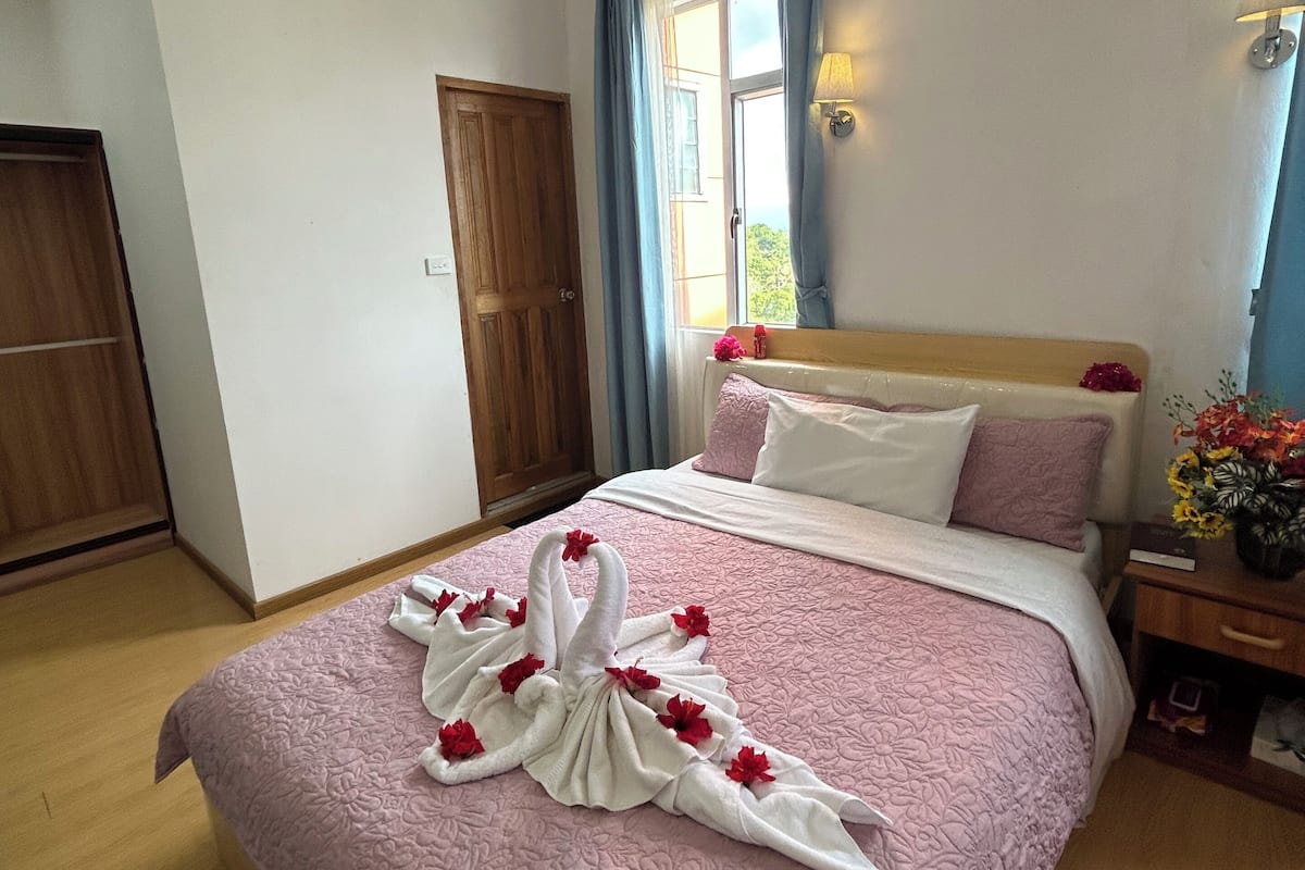 Ein Hotelzimmer mit einem großen Bett, einem Holzschrank, einem Fenster mit Vorhängen und einem Nachttisch mit Lampe.