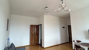 A spacious living area with a grey sofa, wooden flooring, a dining table with chairs, a ceiling fan, and a chandelier.