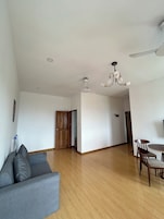 Uma sala de estar espaçosa com sofá cinza, piso de madeira, mesa de jantar com cadeiras, ventilador de teto e lustre.