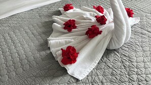 A neatly made bed with a white duvet, grey pillows, and a decorative towel shaped like a swan with red flowers.