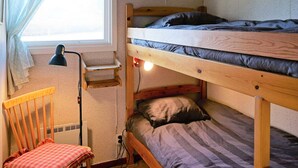 Un lit superposé avec un bureau et une chaise, une fenêtre avec des rideaux et une lampe.