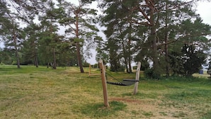 Un hamac est suspendu dans un espace verdoyant d’un parc, avec des arbres en arrière-plan.