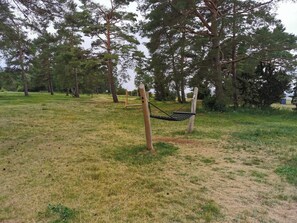 Una hamaca colgada en un parque con césped y árboles al fondo.