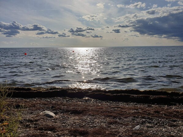 A coastal landscape with a rocky shoreline, calm sea, and a partly cloudy sky.