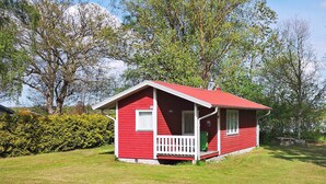 A small, red wooden house with a white porch and a green trash bin. - 5 Person Holiday Home in Morbylanga (Morbylanga)