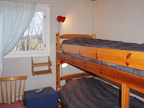 A bunk bed with a desk and chair, a window with curtains, and a red lamp.
