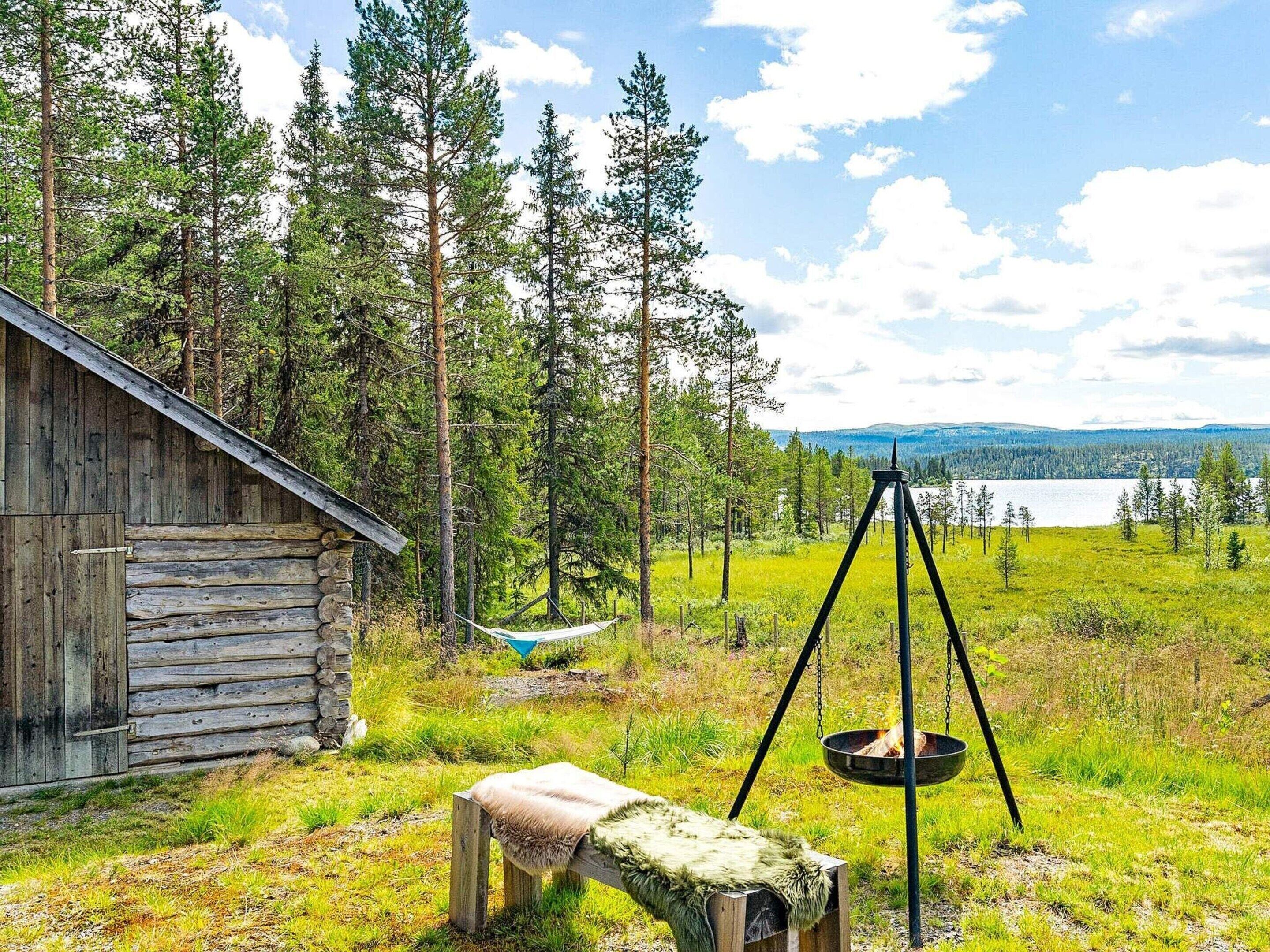 Eine rustikale Holzhütte mit Stein Fundament, einer Hängematte, einer hängenden Feuerstelle und einer Bank mit Felldecke.