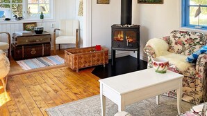 Un salon chaleureux avec un poêle à bois, un canapé à motifs floraux et un fauteuil blanc.