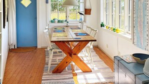 Un coin repas avec une table en bois, des chaises blanches, un tapis à motifs et une fenêtre donnant sur un paysage verdoyant.
