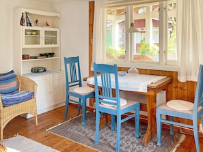 A cozy room with a wooden table and four blue chairs, a wicker chair with a striped cushion, and a white cabinet with glass doors.