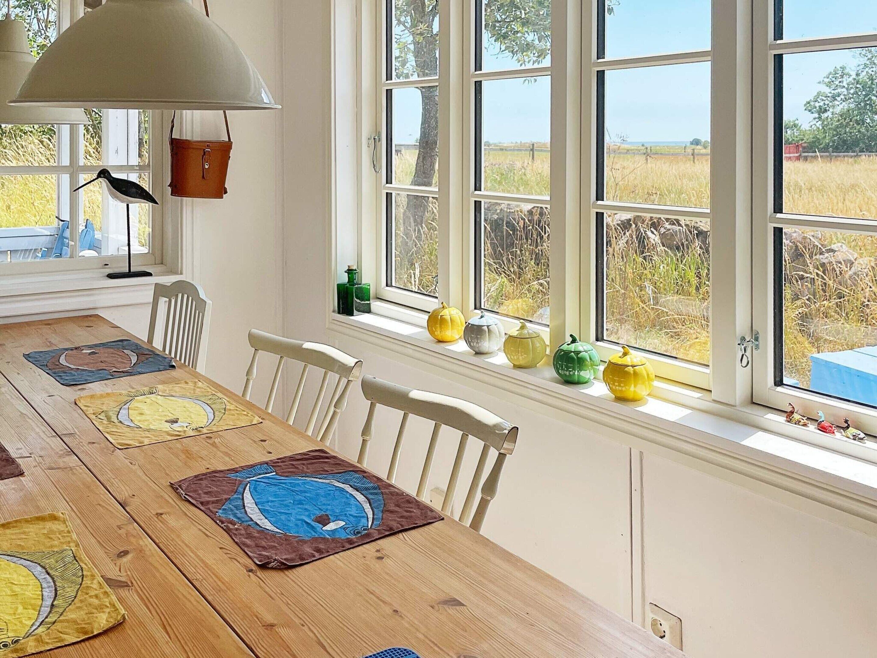 A dining area with a wooden table, white chairs, and a window with a view of a field.