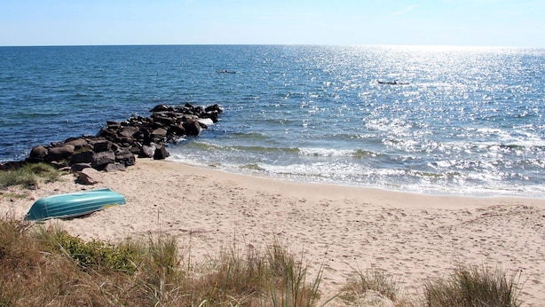 En strand med en vågbrytare av sten, en båt på sanden och havet.