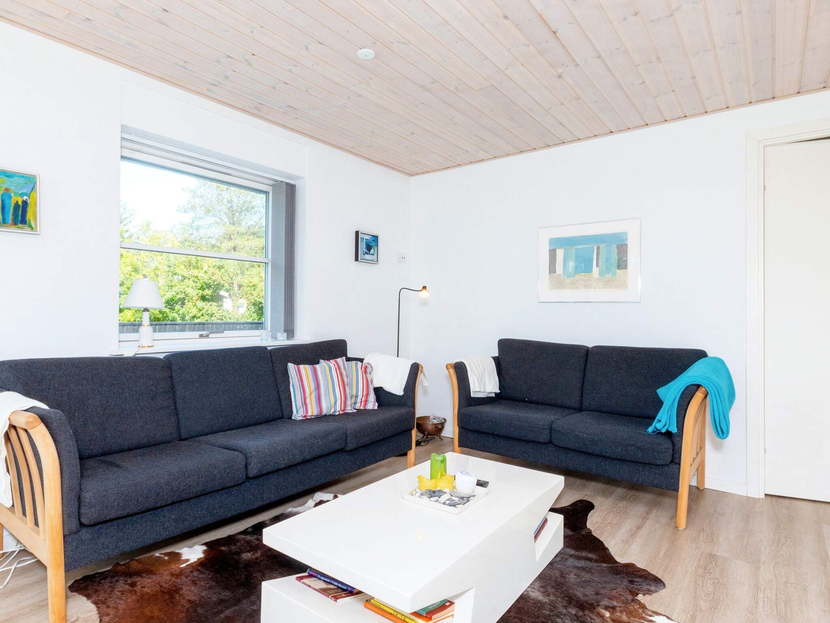 Una sala de estar moderna con dos sofás oscuros, una mesa de centro blanca y un ventanal grande.