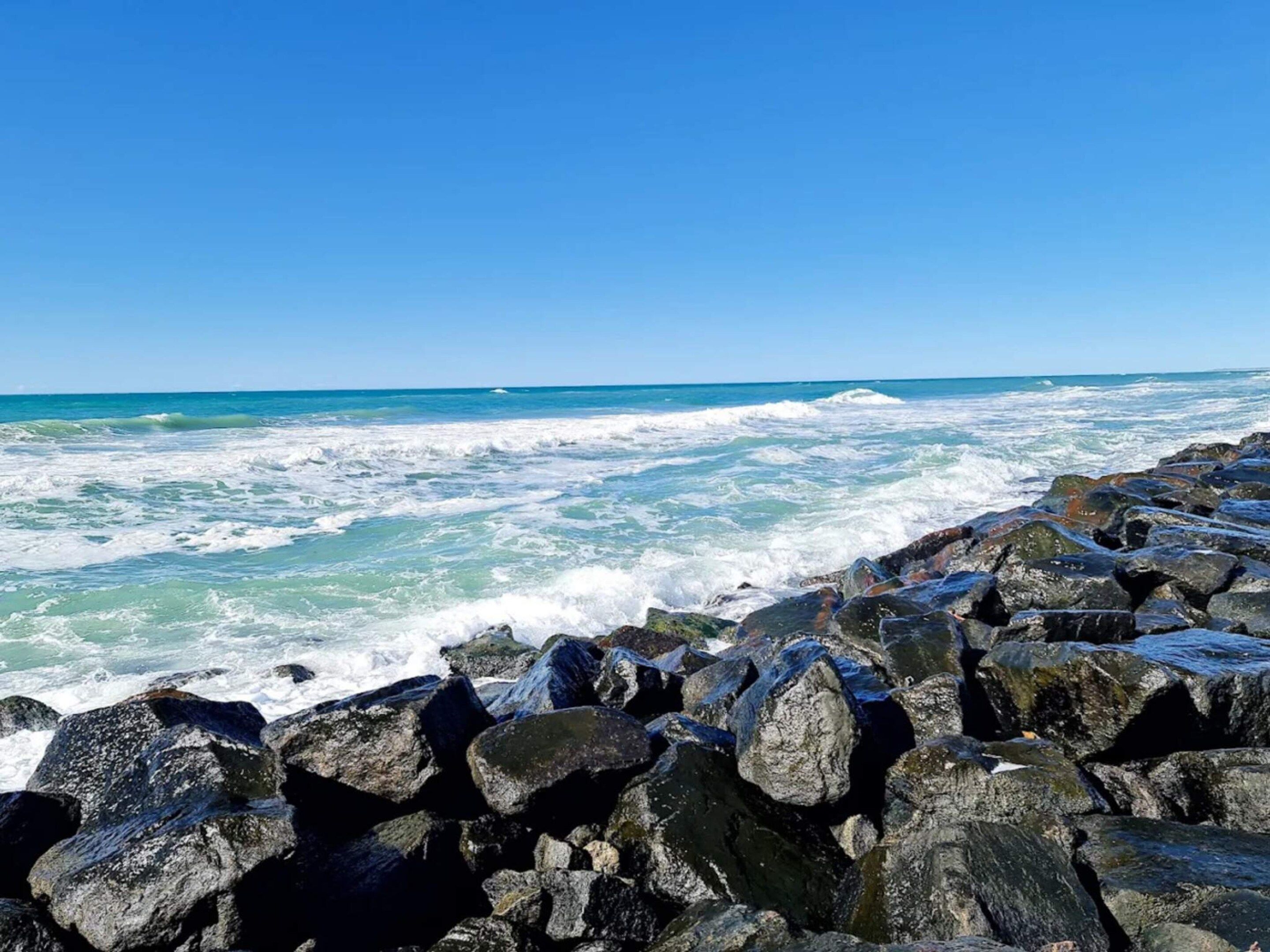 A rocky shoreline with waves crashing against the rocks under a clear blue sky.