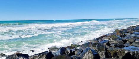 A rocky shoreline with waves crashing against the rocks under a clear blue sky.
