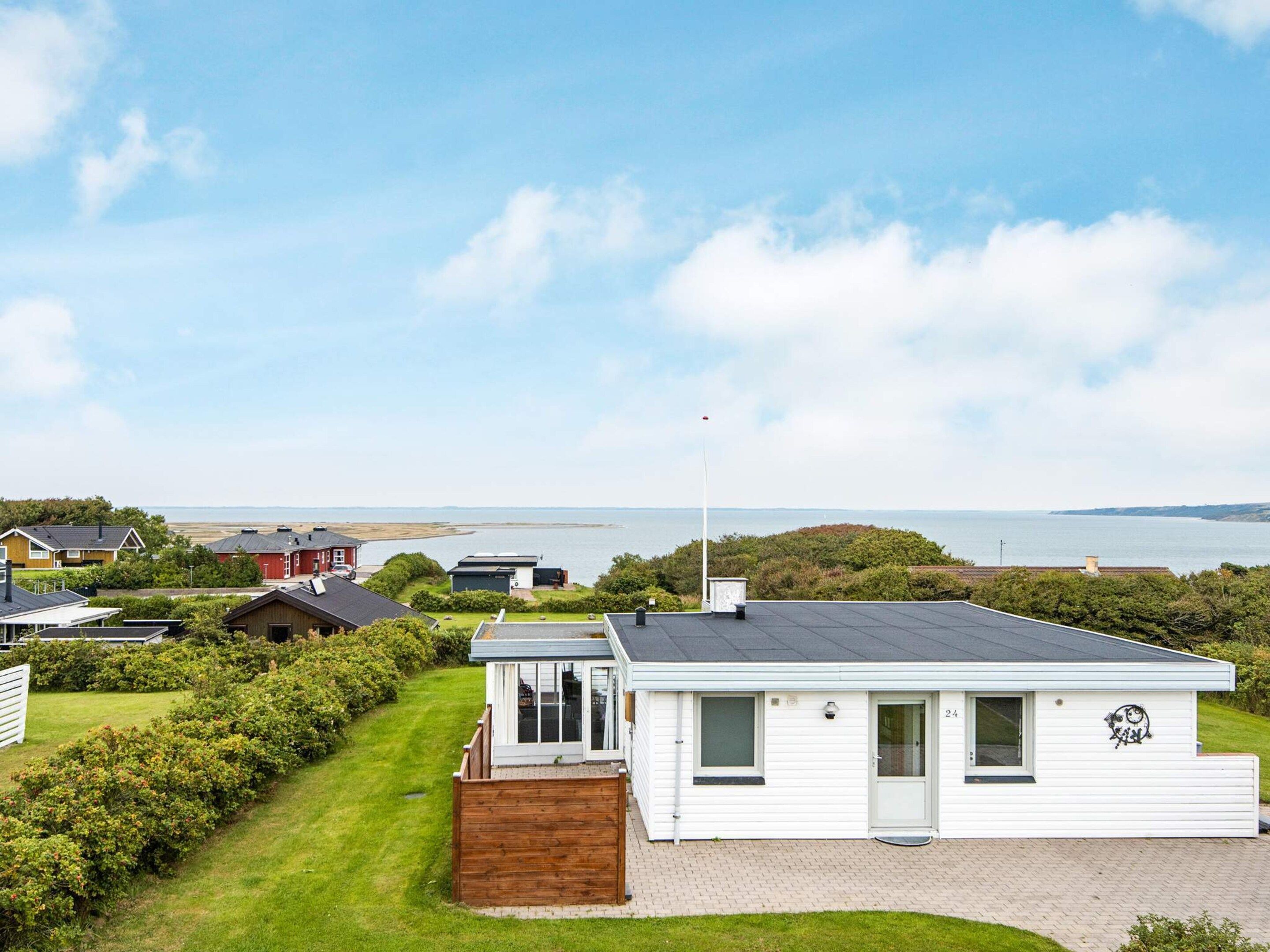 A white mobile home with a small deck, a garage, and a view of the sea.