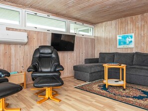 A room with a wooden ceiling, a black leather chair, a grey sofa, a small wooden side table, and a patterned rug. - 7 Person Holiday Home in Lemvig (Lemvig)