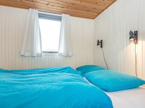 Une pièce avec un lit, une fenêtre avec des rideaux et une lampe fixée au mur.