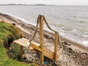 A wooden bench with a rope backrest by a rocky beach. - 7 Person Holiday Home in Lemvig (Lemvig)