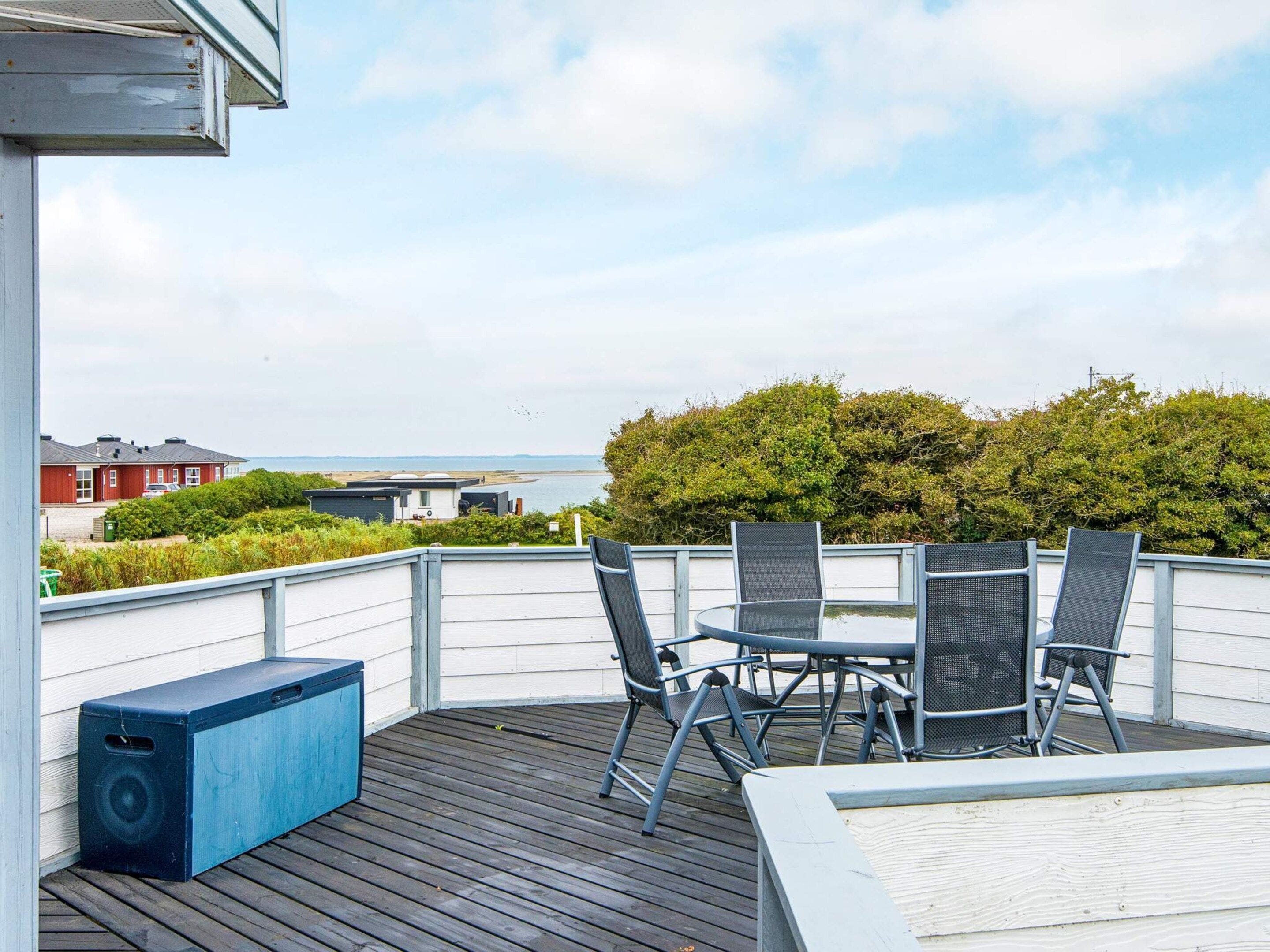En terrasse med udendørs møbler og en højttaler, med udsigt over en strand og boliger.